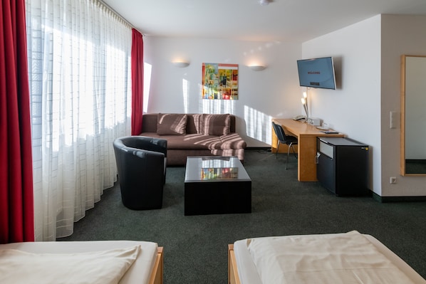 A hotel room with a bed, a sofa, a desk, a TV, and a trash bin.