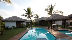 A swimming pool with wooden deck, thatched-roof huts, and palm trees. - Atins Charme Chales (Barreirinhas)