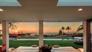 Un comedor con vistas a la puesta de sol sobre una piscina y el paisaje.