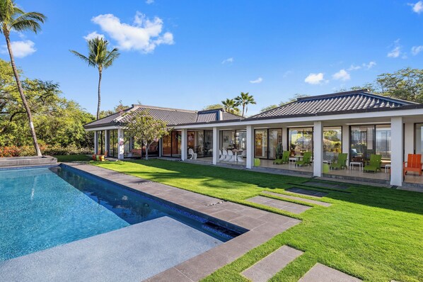 Una casa moderna con piscina, un patio con mobiliario exterior y un césped bien cuidado.