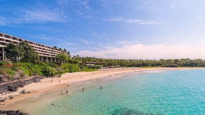 Un hotel frente a la playa con aguas turquesas cristalinas, una playa de arena y abundante vegetación.