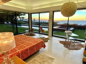 Un dormitorio moderno con una cama grande, vista al océano y un muro de cristal.