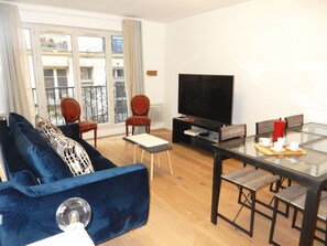 A modern living room with a blue sofa, two red chairs, a glass dining table with four chairs, a flat-screen TV, and a coffee maker. - Central charming Apt South butte Montmartre up to 7 people (Paris)