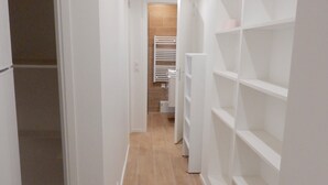 A narrow hallway with white shelving units on both sides and a tiled floor.