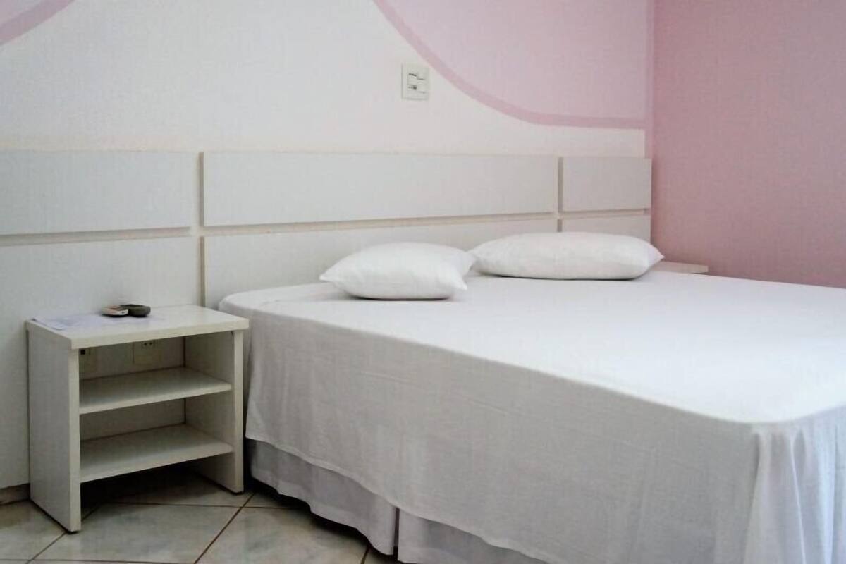 Een slaapkamer met een bed, twee kussens, een nachtkastje en een plank.