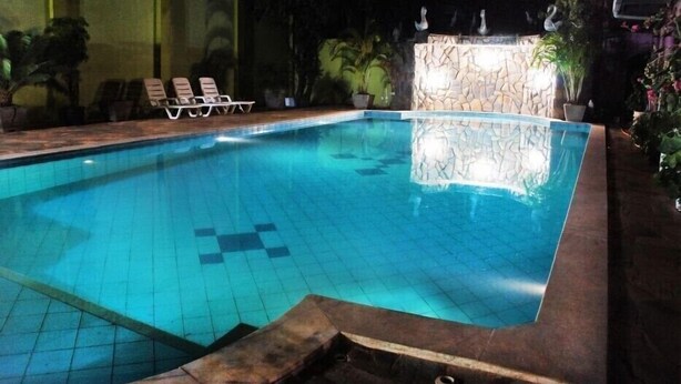 A swimming pool with tiled flooring and a stone wall in the background.
