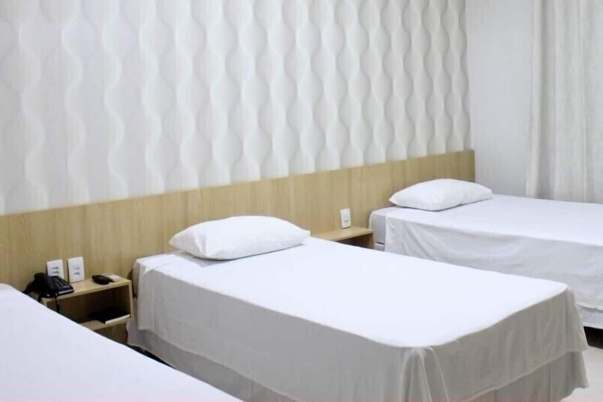 Een hotelkamer met twee enkele bedden, een houten hoofdbord, een nachtkastje met een telefoon, en een muur met een golvend patroon.