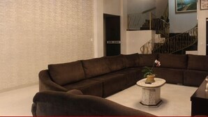 A modern living room with a large L-shaped sectional sofa, a round coffee table with a plant, and a staircase with a metal railing in the background.