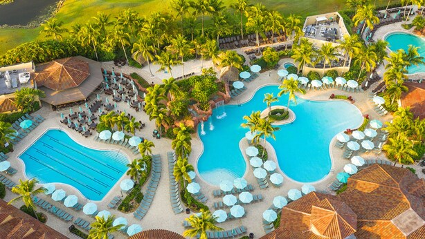 An aerial view of a resort with multiple swimming pools, sun loungers, and palm trees.