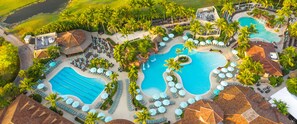 Eine Vogelperspektive eines Resorts mit mehreren Schwimmbecken, Liegestühlen und Palmen.