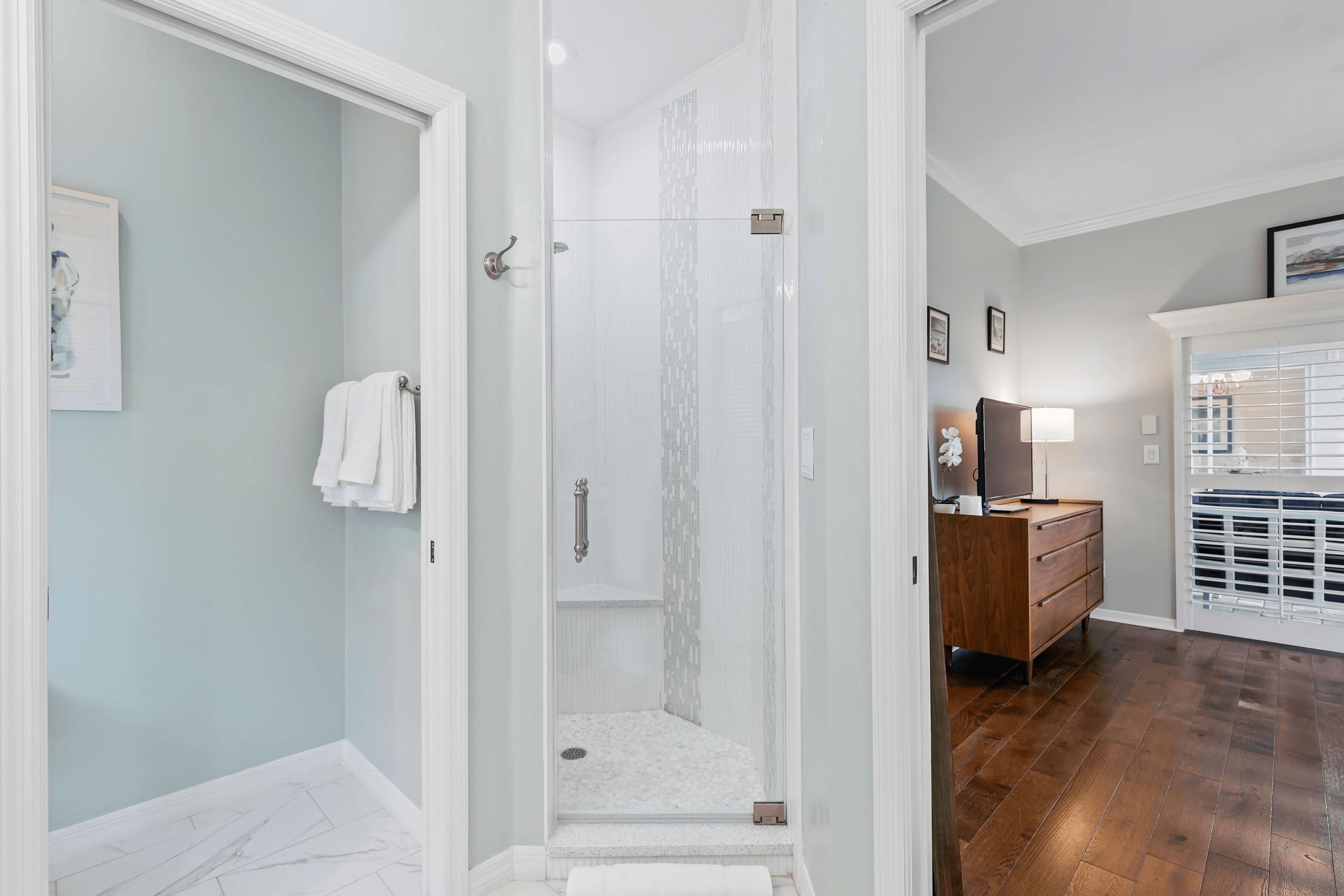 Un bagno moderno con doccia vetrata, un mobile bagno in legno e un pavimento piastrellato di bianco.