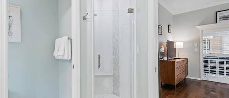 Un bagno moderno con doccia vetrata, un mobile bagno in legno e un pavimento piastrellato di bianco.