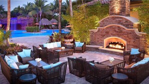 An outdoor patio area with wicker furniture, a pool, and a stone fireplace.