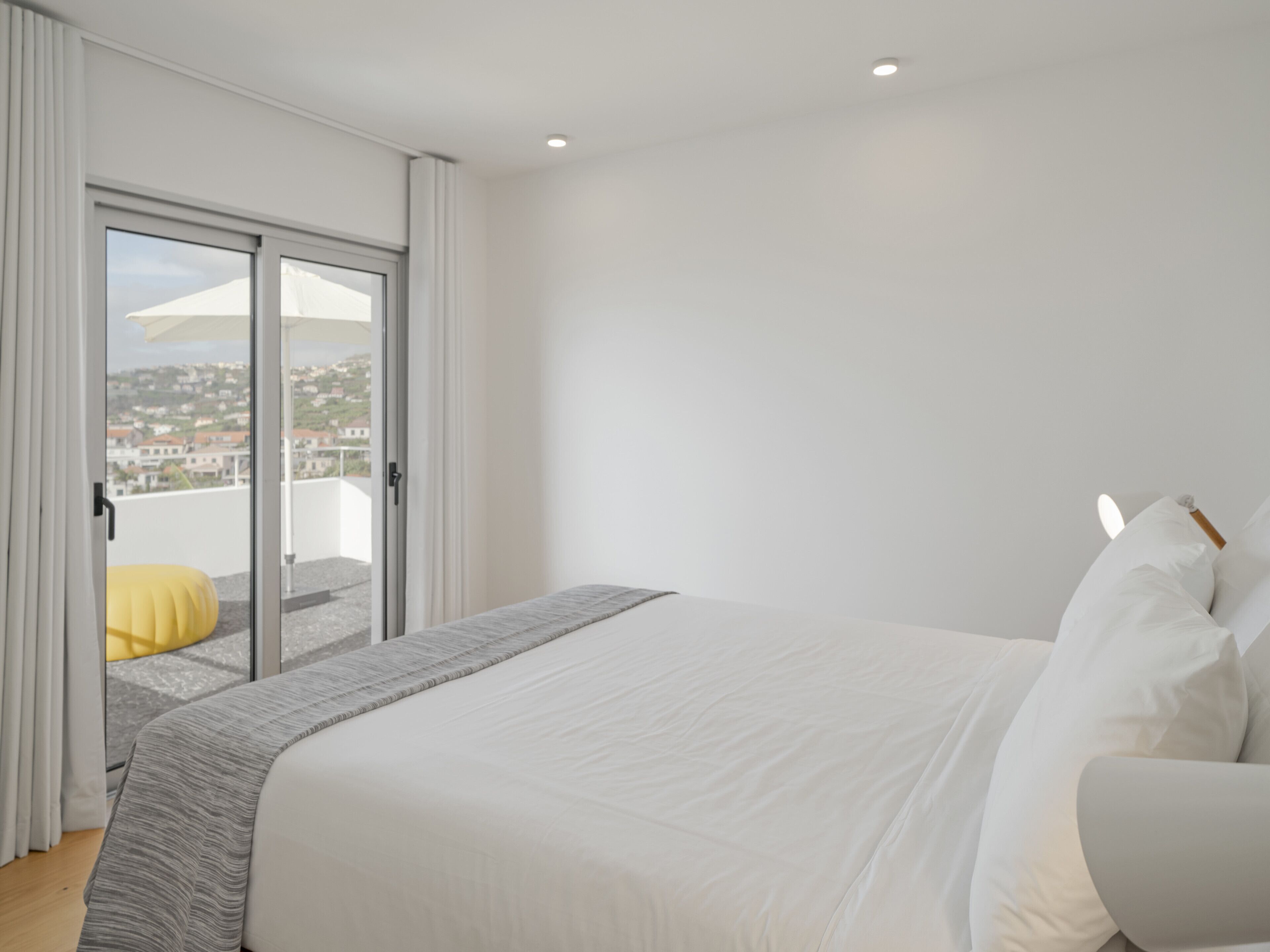 Une chambre avec un grand lit, une porte-fenêtre coulissante donnant sur un balcon et une vue sur la ville.