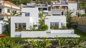A modern residential area with white buildings, a swimming pool, and lush greenery including banana trees.