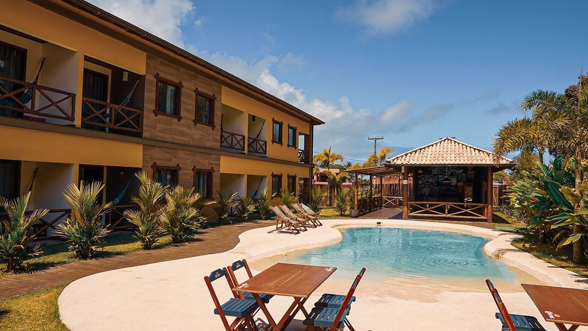 A hotel with a pool, lounge chairs, and a covered area.