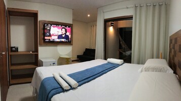 Una habitación de hotel con una cama, un televisor montado en la pared, un escritorio y una silla.