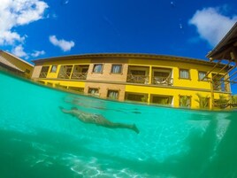 Una piscina con una persona nadando, rodeada por un edificio amarillo con balcones.