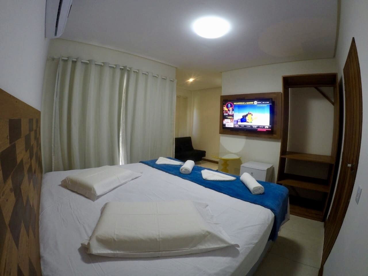 Una habitación de hotel con una cama grande, un televisor montado en la pared y un escritorio con una silla.