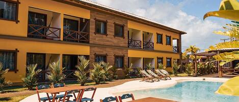 A hotel with a pool, outdoor seating, and a tropical garden.