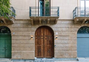 A building facade with two large wooden doors, a balcony with metal railings, and a stone wall.