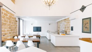 Een moderne keuken met een achterwand van steen, een centraal eiland en een eethoek met witte stoelen en een houten tafel.