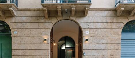 An entrance with a stone archway, a green door, and a balcony with metal railings.