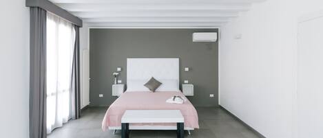 A modern bedroom with a large bed, bedside tables, a bench, and a window with curtains.