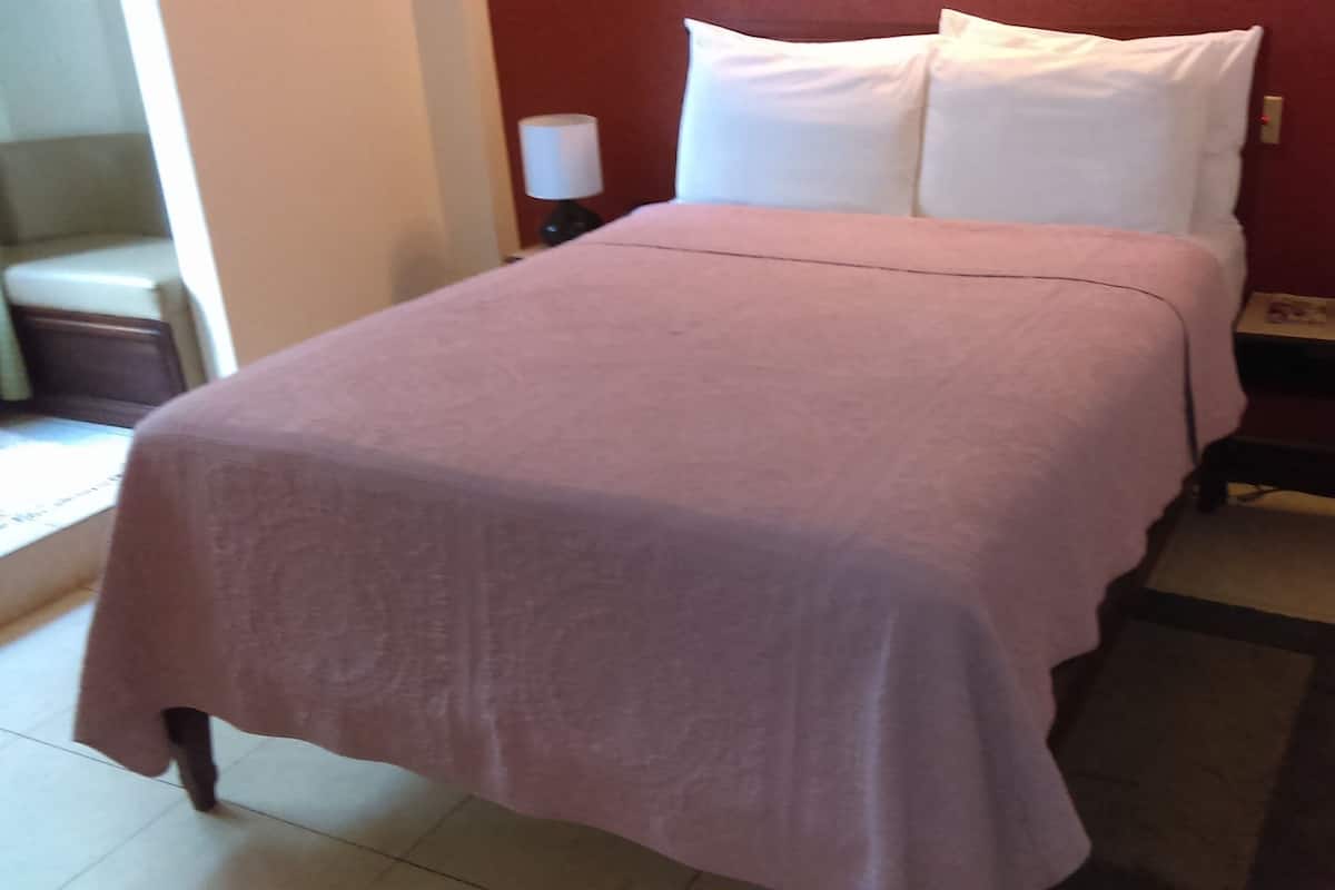 A neatly made bed with a pink bedspread, two white pillows, and two bedside lamps on either side.