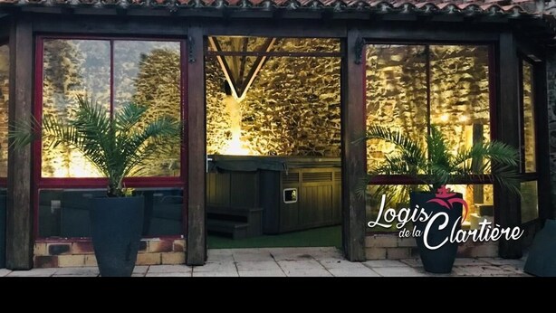 Un espacio al aire libre cubierto con ventanas amplias, plantas en macetas y una pared de piedra al fondo.