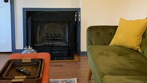 A living room with a fireplace, a green sofa with a yellow pillow, a wooden side table with a remote control, a mirror, and a framed picture on the wall. - Pete's Place: Forest retreat near wineries, Blue Ridge School, and Shenandoah NP (Stanardsville)