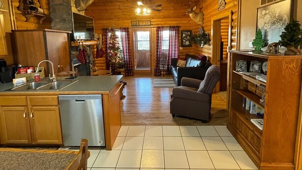 A cozy cabin interior with a wooden interior, a fireplace, a dining area, and a living room with a sofa and armchairs. - 2 bed Log Cabin, w/2 Jacuzzi, 1 mi to SDC, pool, nature trails, private lake (Reeds Spring)