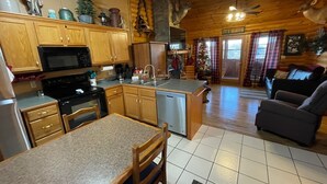 A cozy cabin-style kitchen with wooden cabinets, a stainless steel refrigerator, and a dining area with a table and chairs. - 2 bed Log Cabin, w/2 Jacuzzi, 1 mi to SDC, pool, nature trails, private lake (Reeds Spring)
