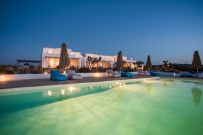 Una villa moderna con piscina, mobiliario exterior e iluminación en la entrada.