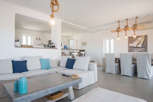 Una sala de estar moderna con un amplio sofá en forma de L, una mesa de centro y una zona de comedor con sillas y una mesa.
