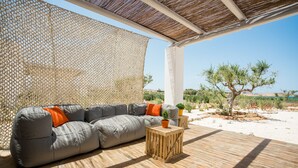 Un área de estar al aire libre con un sofá gris, mesas de madera y plantas en macetas.