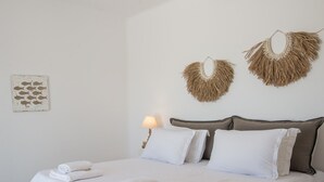 Una cama bien hecha con sábanas y toallas blancas, una lámpara de noche y decoración en la pared.