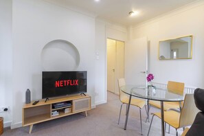 Uma sala de estar moderna com televisão de tela plana, uma mesa de jantar de vidro e um sofá.