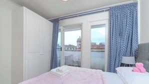 Une chambre d’hôtel avec un lit, une chaise, une lampe et une vue sur le paysage urbain par la fenêtre.