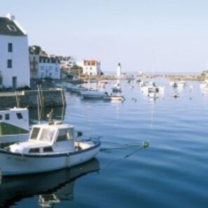 A marina with several boats docked, a white building with a sloped roof, and a lighthouse in the background.