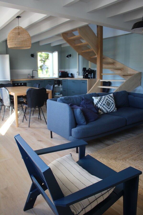 A modern living space with a blue sofa, a wooden dining table, and a staircase leading to an upper level.