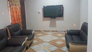 A living room with two sofas, a flat-screen TV mounted on the wall, and patterned floor tiles. - Private Executive Apartments (Accra)