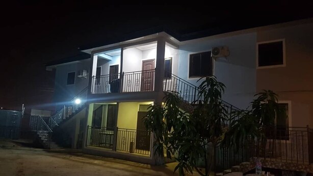 A two-story building with a balcony on the upper floor, a staircase leading to the entrance, and a gated driveway. - Private Executive Apartments (Accra)