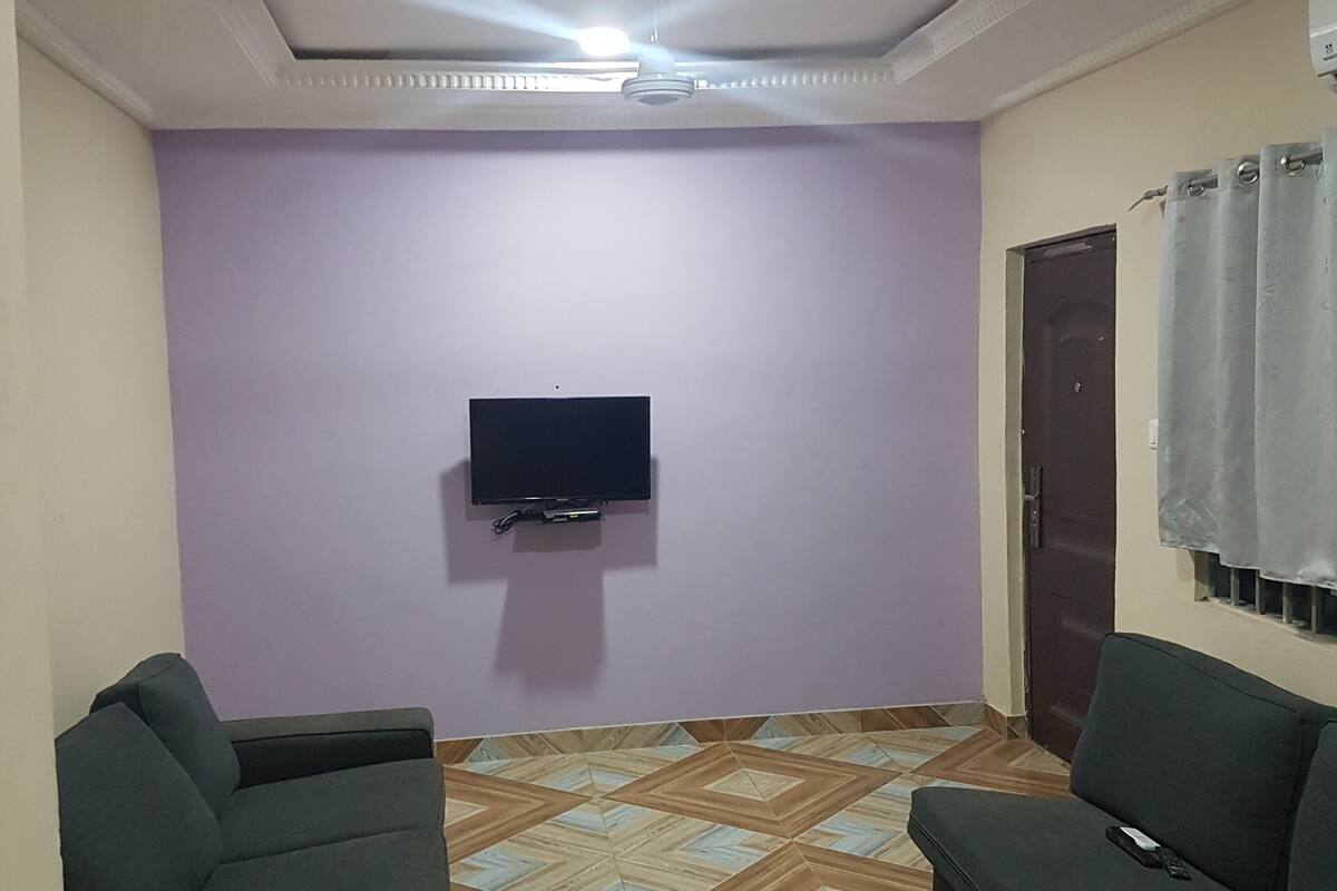 A living room with two sofas, a flat-screen TV mounted on the wall, patterned wooden flooring, and a ceiling light.