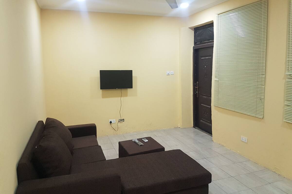 A living room with a flat-screen TV mounted on the wall, a ceiling fan, and a door with a window with blinds.