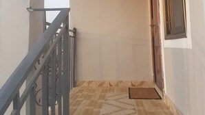 A corridor with a tiled floor, a metal railing, and a door with a window. - Private Executive Apartments (Accra)