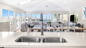A modern kitchen with a stainless steel sink, a dining area with a wooden table and chairs, and a view of the ocean through large windows. - Sea Gem: Beach/Slp 10 Adults plus children/Amenities (St. Augustine)