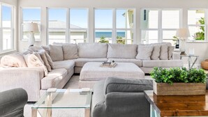 A spacious living room with a large L-shaped sectional sofa, a glass coffee table, and a view of the ocean through large windows. - Sea Gem: Beach/Slp 10 Adults plus children/Amenities (St. Augustine)