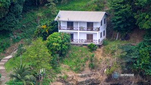 A two-story white house with a balcony, surrounded by lush greenery and a steep hillside. - Tranquil and Peaceful Parlatuvier 2 (Parlatuvier)