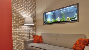 A modern living room with a brick wall, a sofa with orange cushions, a white coffee table with a glass vase, and a fish tank on the wall. - Charming House in Old Town Desenzano (Desenzano del Garda)